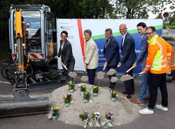 Spatenstich mit Stadtwerke-Geschäftsführerin Julia Teige (l.), Ministerin für Infrastruktur und Digitales des Landes Sachsen-Anhalt Dr. Lydia Hüskens, Oberbürgermeister Bert Knoblauch (3.v.l.) und MDCC_Geschäftsführer Guido Nienhaus (3.v.r.). © Stadt Schönebeck (Elbe) Sechs Personen schippen Sand vor einem Bagger.
