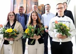 Sechs Personen stehen auf der Treppe im Rathaus, davon drei Auszubildende mit Blumenstrauß.