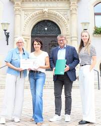 Eim Mann und drei Frauen stehen vor dem Schönebecker Rathaus und halten einen symbolischen Spendenscheck.