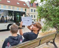 Zwei Schüler sitzen auf einer Bank und wollen Busse zählen.