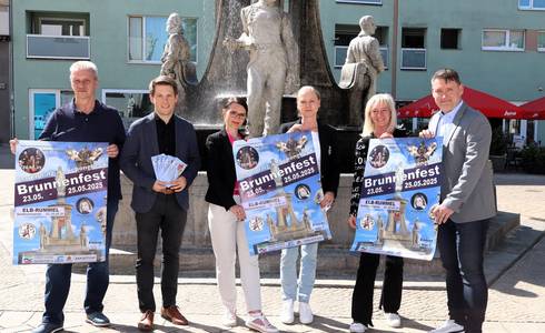 Sechs personen stehen vor einem Brunnen und präsentieren Plakate für die Veranstaltung.