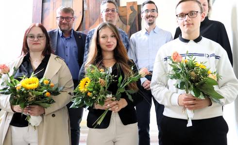 Sechs Personen stehen auf der Treppe im Rathaus, davon drei Auszubildende mit Blumenstrauß.