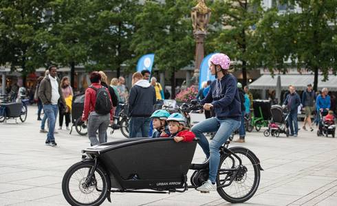 Unterschiedliche Lastenräder können getestet werden. © Cargobike-Roadshow / Andreas Lörcher Ein Mann transportiert zwei Kinder mit einem Lastenrad.